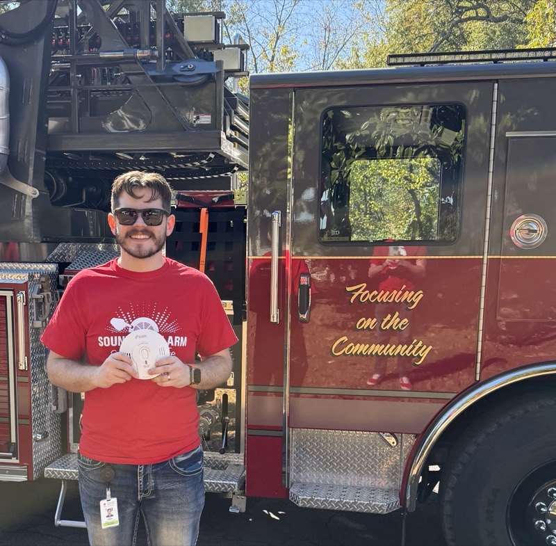 Guy holding a smoke alarm next to a fire truck during Sound the Alarm event